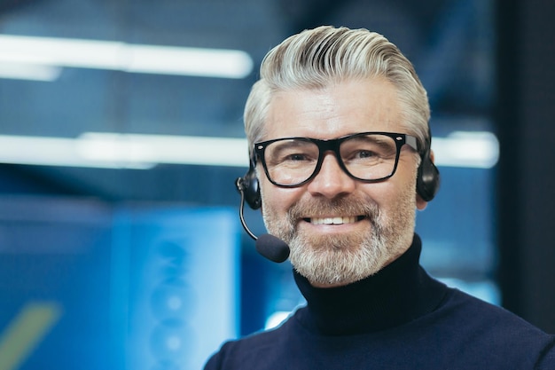 Retrato de um homem bonito grisalho em óculos e um fone de ouvido com um negócio de alto-falante de microfone