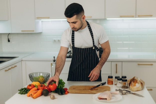 Retrato de um homem bonito na cozinha Um homem vestido com um avental preto Pique legumes para cozinhar