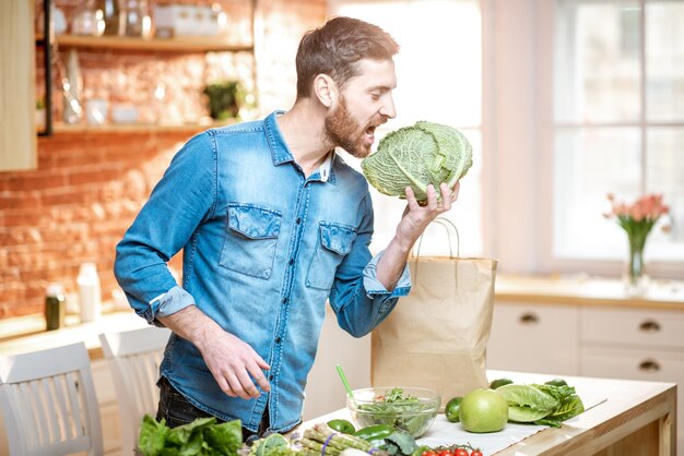 Retrato de um homem bonito, segurando a cabeça de repolho na cozinha. Conceito de comida vegana saudável