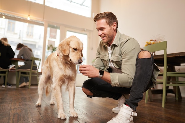 Retrato de um homem bonito sorridente com seu cachorro sentado no chão em um café com um golden retriever dando