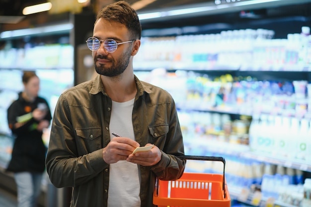 Retrato de um homem bonito sorridente fazendo compras no supermercado escolhendo produtos alimentares da prateleira