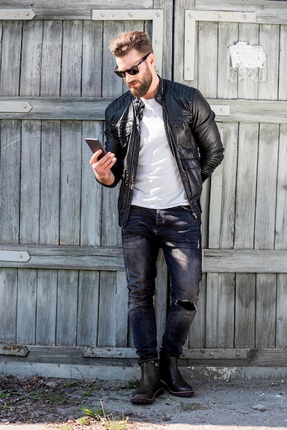 Retrato de um homem bonito vestido de camiseta branca, jaqueta e jeans com telefone no fundo de madeira velho