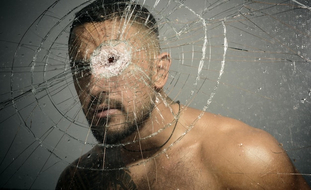 Retrato de um homem brutal com cara séria Homem gangster Perigoso criminoso hooligan em vidro de bala rachado