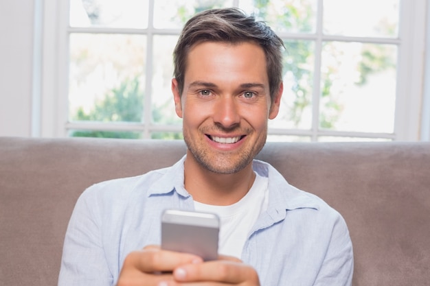 Retrato de um homem casual lendo mensagem de texto no sofá