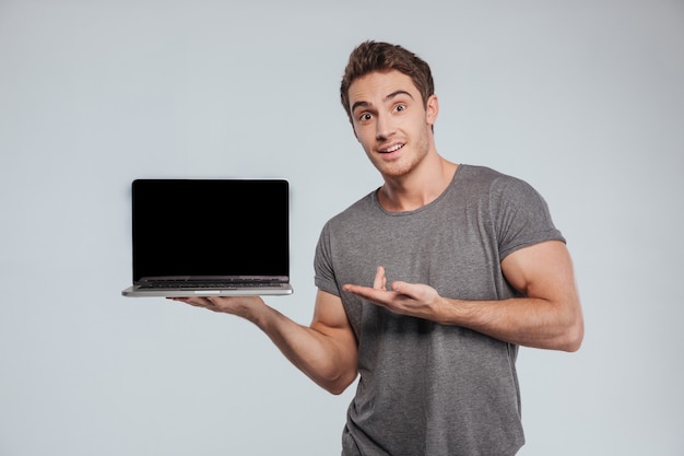 Foto retrato de um homem casual surpreso apontando na tela em branco do laptop em branco