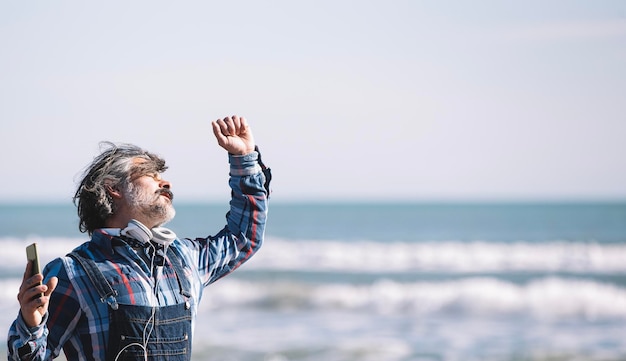 Retrato de um homem caucasiano alegre em um chapéu desfrutando na praia em um dia ensolarado no inverno