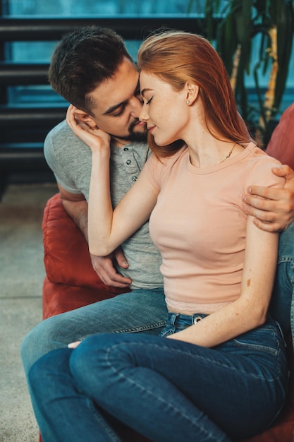 Foto retrato de um homem caucasiano beijando uma mulher de coração vermelho enquanto está sentado na poltrona afetuosa feminina r ...