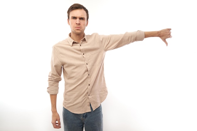 Retrato de um homem caucasiano descontente mostrando os polegares para baixo isolados no fundo branco do estúdio Não aprova algo que não gosta