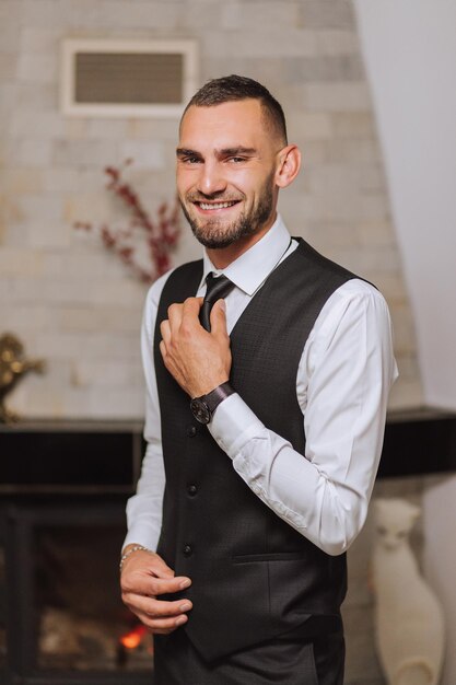 Retrato de um homem com camisa branca, colete e gravata preta em uma sala com luz natural o noivo está se preparando para o casamento o homem está vestindo uma camisa branca noivo elegante