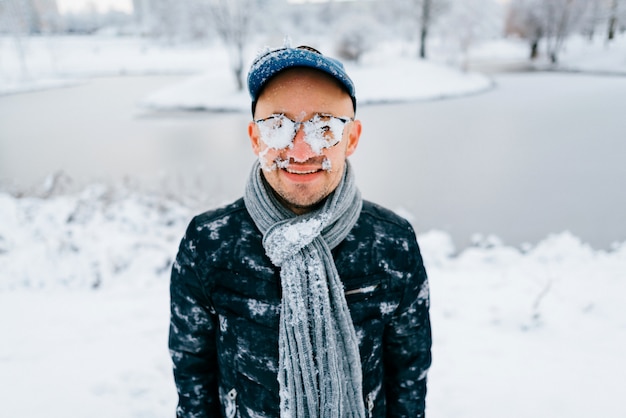 Retrato de um homem com neve no rosto ao ar livre, com rosto sorridente no dia de inverno nevado na natureza.