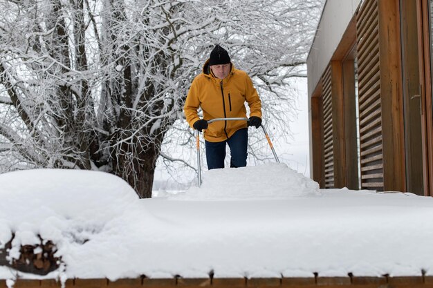 Retrato de um homem com roupas de inverno com pá de neve limpando neve do terraço do prédio