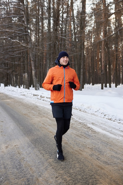 Retrato de um homem com roupas esportivas brilhantes, correndo por uma floresta de inverno. dia gelado