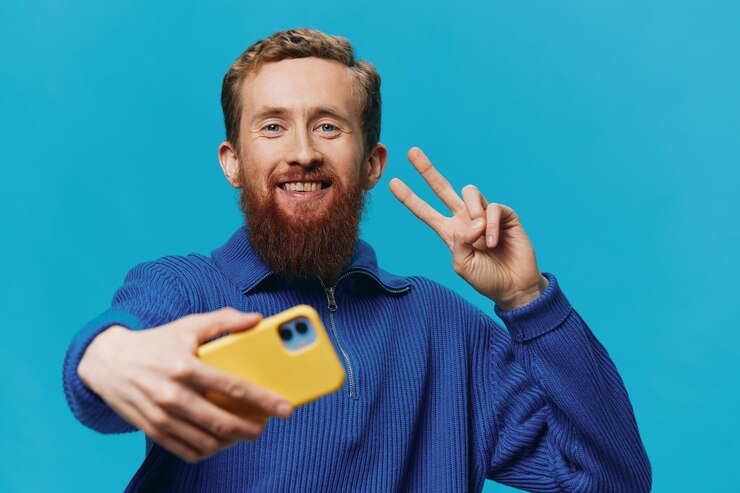 Foto retrato de um homem com um telefone em suas mãos blogueiro tira selfies em um fundo azul comunicando estilo de vida de mídia social on-line