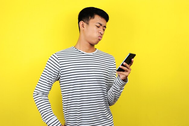 Retrato de um homem confuso olhando para um smartphone, isolado em um fundo amarelo