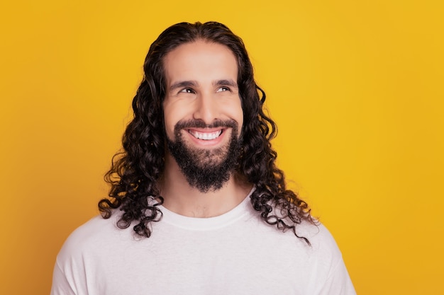 Retrato de um homem curioso e pensativo, sorriso branco e brilhante, olhar para o espaço em branco no fundo amarelo