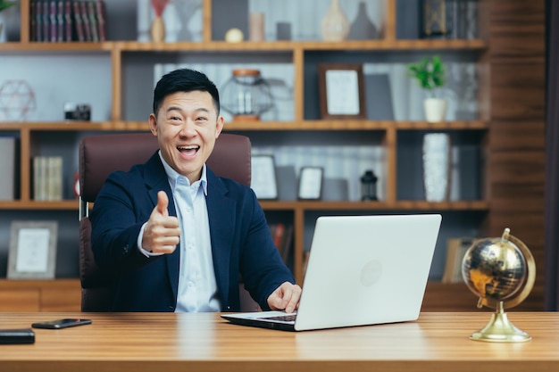 Retrato de um homem de advogado político asiático bem sucedido trabalhando na mesa no escritório clássico olhando para a câmera e sorrindo