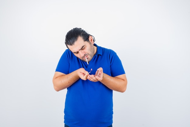 Retrato de um homem de meia-idade acendendo um cigarro com fósforos em uma camiseta polo e olhando de frente para o foco