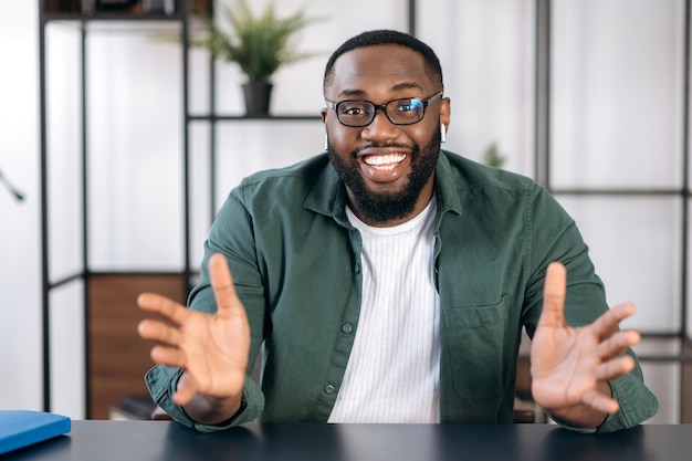 Foto retrato de um homem de negócios afro-americano bem-sucedido e amigável, freelancer, falando durante videoconferência com colegas ou amigos, gestando as mãos e sorrindo, falando sobre planos e estratégias.