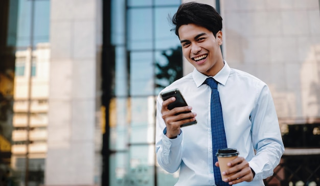 Retrato de um homem de negócios asiático de sorriso feliz Using Mobile Phone na cidade urbana. Estilo de vida das pessoas modernas. Olhando para a câmera. Edifício moderno como pano de fundo