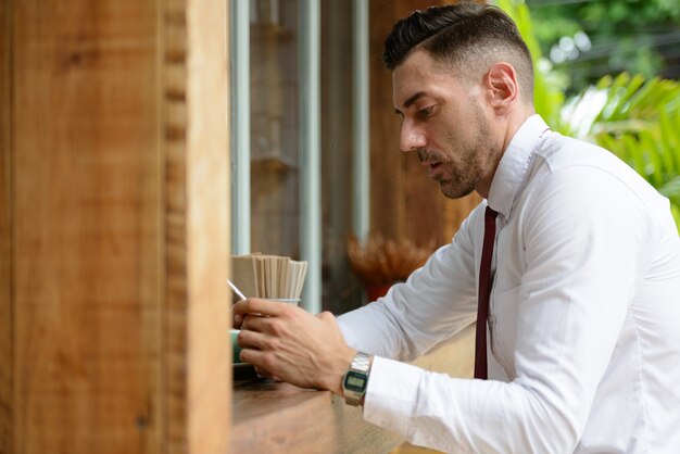 Retrato de um homem de negócios bonito com barba por fazer relaxando no café ao ar livre