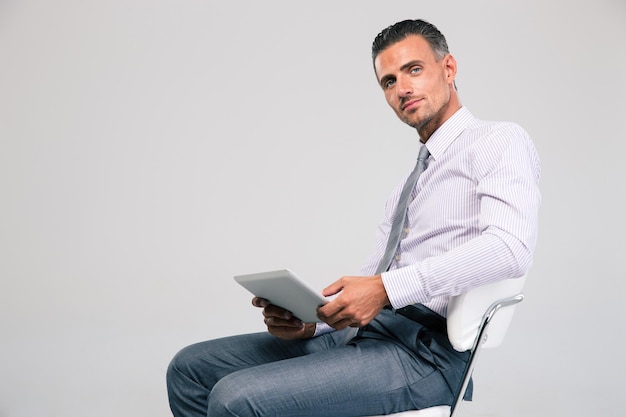 Retrato de um homem de negócios bonito sentado na cadeira do escritório com um computador tablet isolado