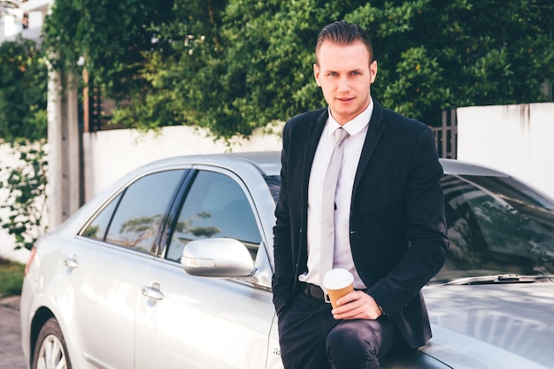 Retrato de um homem de negócios de pé com um carro na estrada