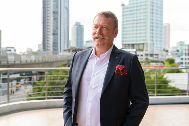 Retrato de um homem de negócios sênior bonito com bigode contra a vista da cidade