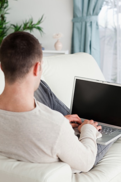 Retrato de um homem deitado no sofá para usar um laptop