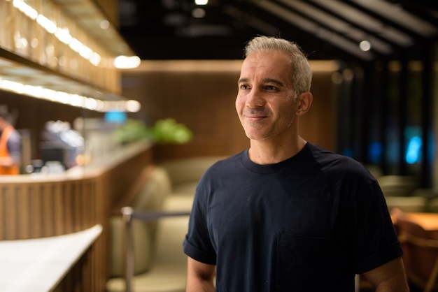 Retrato de um homem dentro da cafeteria à noite, sorrindo e pensando, foto horizontal