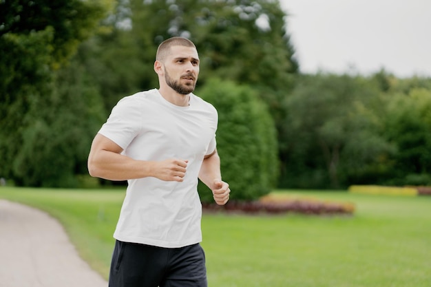 Retrato de um homem desportivo com cabelo escuro correndo em uma esteira em uma camiseta branca praticando esportes