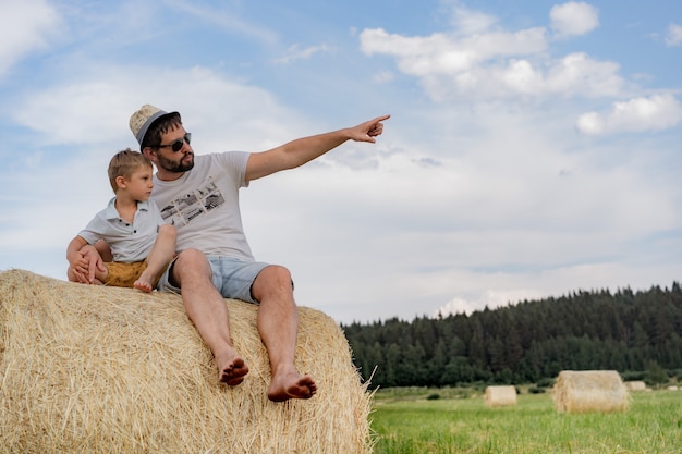 Retrato de um homem e seu filho sentado em um palheiro redondo em um campo verde em um dia ensolarado de verão