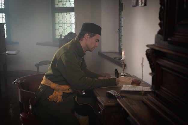 Foto retrato de um homem em um traje medieval. um escriba escreve em uma mesa vermelha. estilo retrô e conceitos históricos de roupas