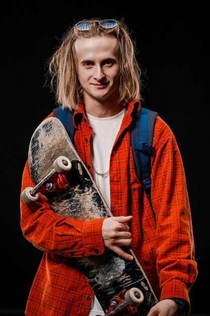 Retrato de um homem estiloso segurando um skate no Studio Close de um skatista sorridente posando em um fundo preto