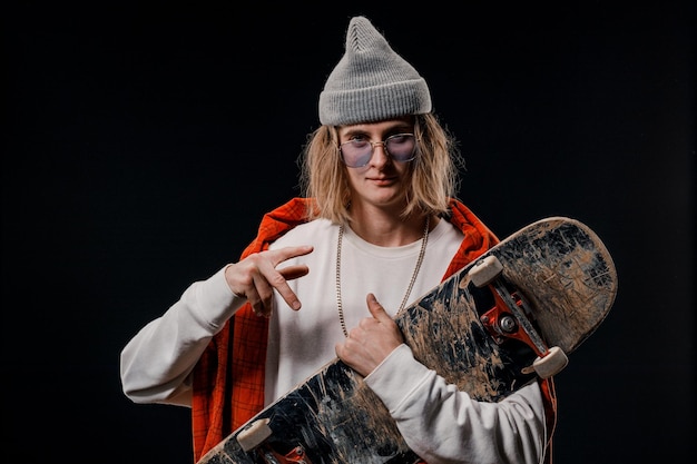 Retrato de um homem estiloso segurando um skate no Studio Close de um skatista sorridente posando em um fundo preto