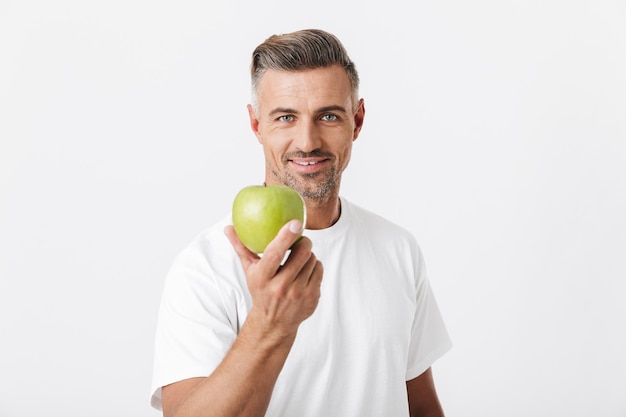 Foto retrato de um homem feliz dos anos 30 com as cerdas posando e segurando uma maçã verde na mão isolada no branco