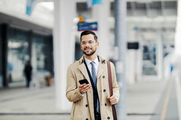 Retrato de um homem feliz e elegante parado na estação de trem e esperando um trem