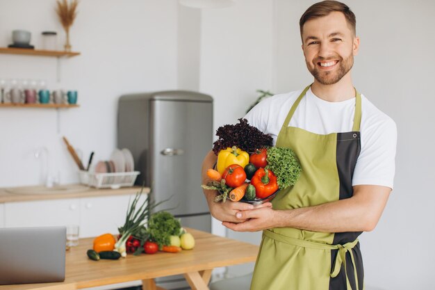 Retrato de um homem feliz segurando um prato de legumes frescos no fundo da cozinha em casa