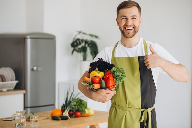 Retrato de um homem feliz segurando um prato de legumes frescos no fundo da cozinha em casa