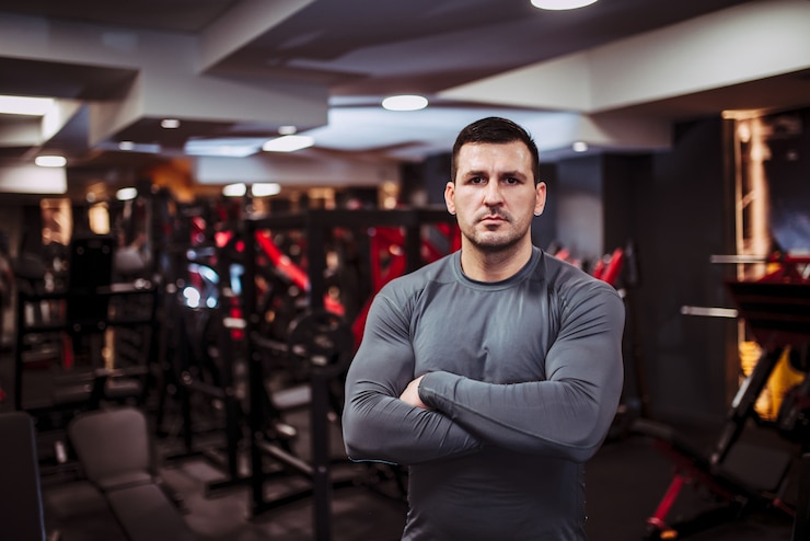 Foto retrato de um homem forte e musculoso no ginásio, em pé com os braços cruzados e olhando para a câmera.