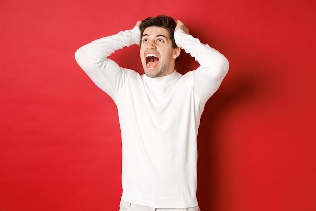 Retrato de um homem frustrado em uma camisola branca gritando em pânico e olhando para o canto superior esquerdo ...