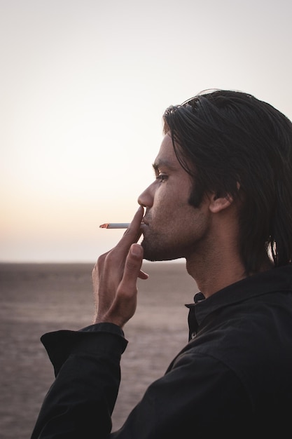 Foto retrato de um homem fumando um cigarro contra um céu claro durante o pôr do sol