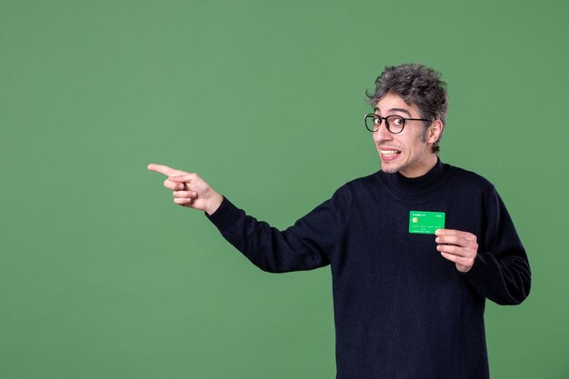 Foto retrato de um homem gênio segurando um cartão de crédito verde em estúdio tiro parede verde