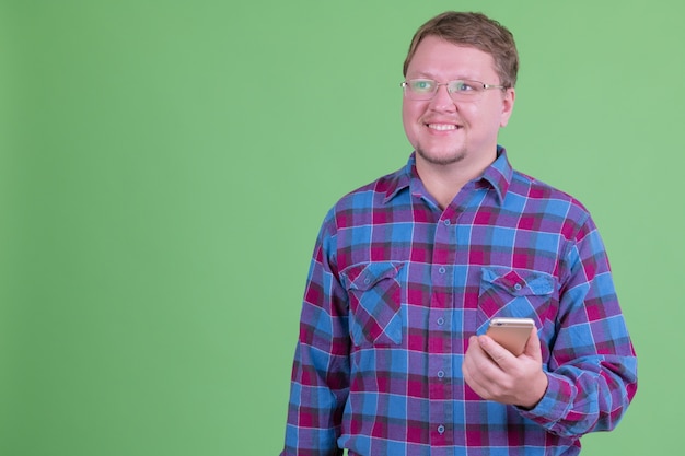 Retrato de um homem hippie barbudo com excesso de peso com óculos contra chroma key ou parede verde