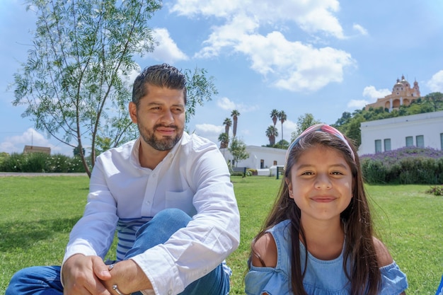 Retrato de um homem hispânico sentado na grama verde com sua filha