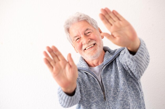 Retrato de um homem idoso alegre em fundo branco olhando para a câmera fazendo um gesto de parada com as mãos