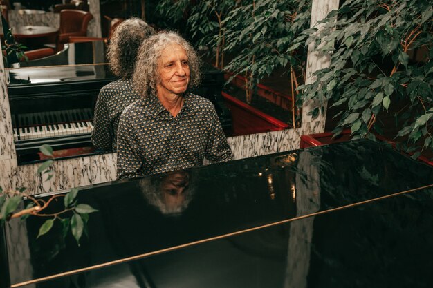 Retrato de um homem idoso, com idade entre 60 e 65 anos, cabelo grisalho encaracolado, sentado ao piano e tocando uma peça musical, focado, melodia injoing