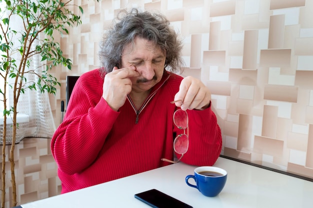 Retrato de um homem idoso esfregando os olhos com a mão de cansaço depois de usar o telefone