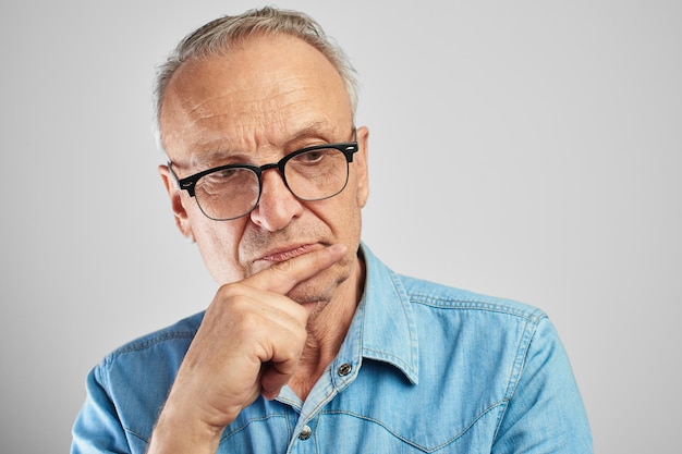 Retrato de um homem idoso moderno elegante de óculos em um fundo branco no estúdio. Chefe sênior pensando em uma pose pensativa