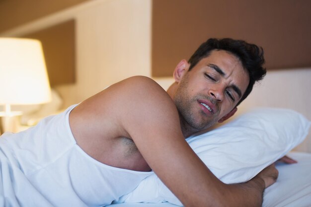 Retrato de um homem infeliz segurando um travesseiro na cama branca Fundo do quarto