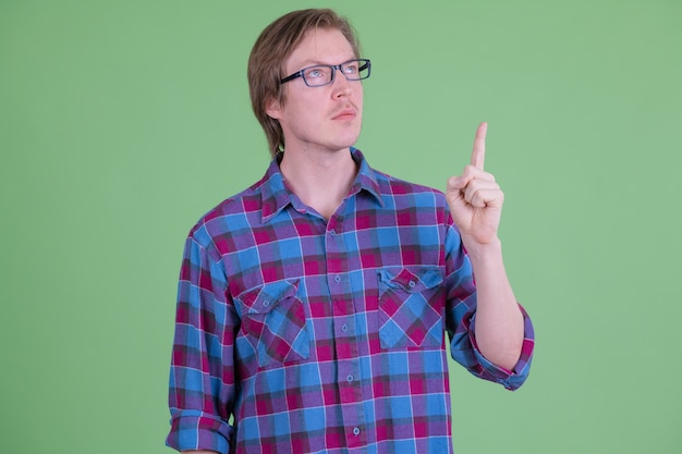 Retrato de um homem jovem e bonito hippie escandinavo com óculos contra chroma key ou parede verde